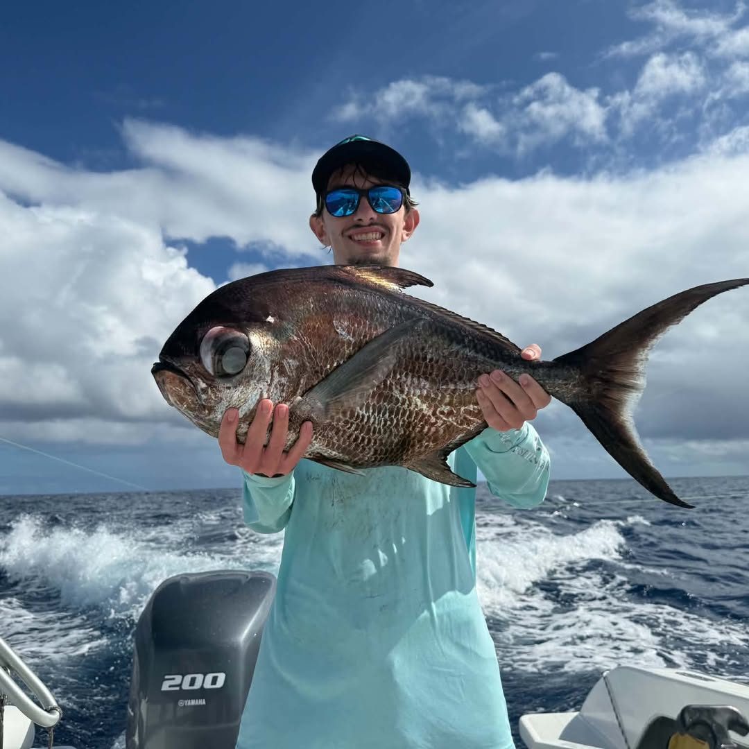 Un jeune pêcheur souriant tient un gros poisson argenté en mer